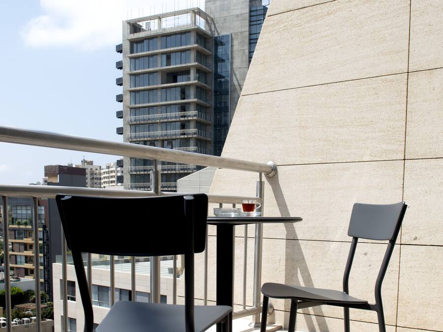Een balkon met twee stoelen en een kleine tafel, met uitzicht op een stadsgezicht met moderne gebouwen.