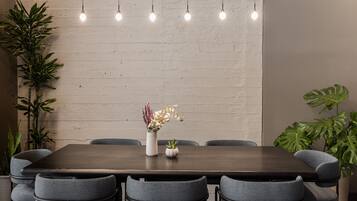 Un comedor con una mesa rectangular, seis sillas grises, focos colgantes y plantas en macetas.