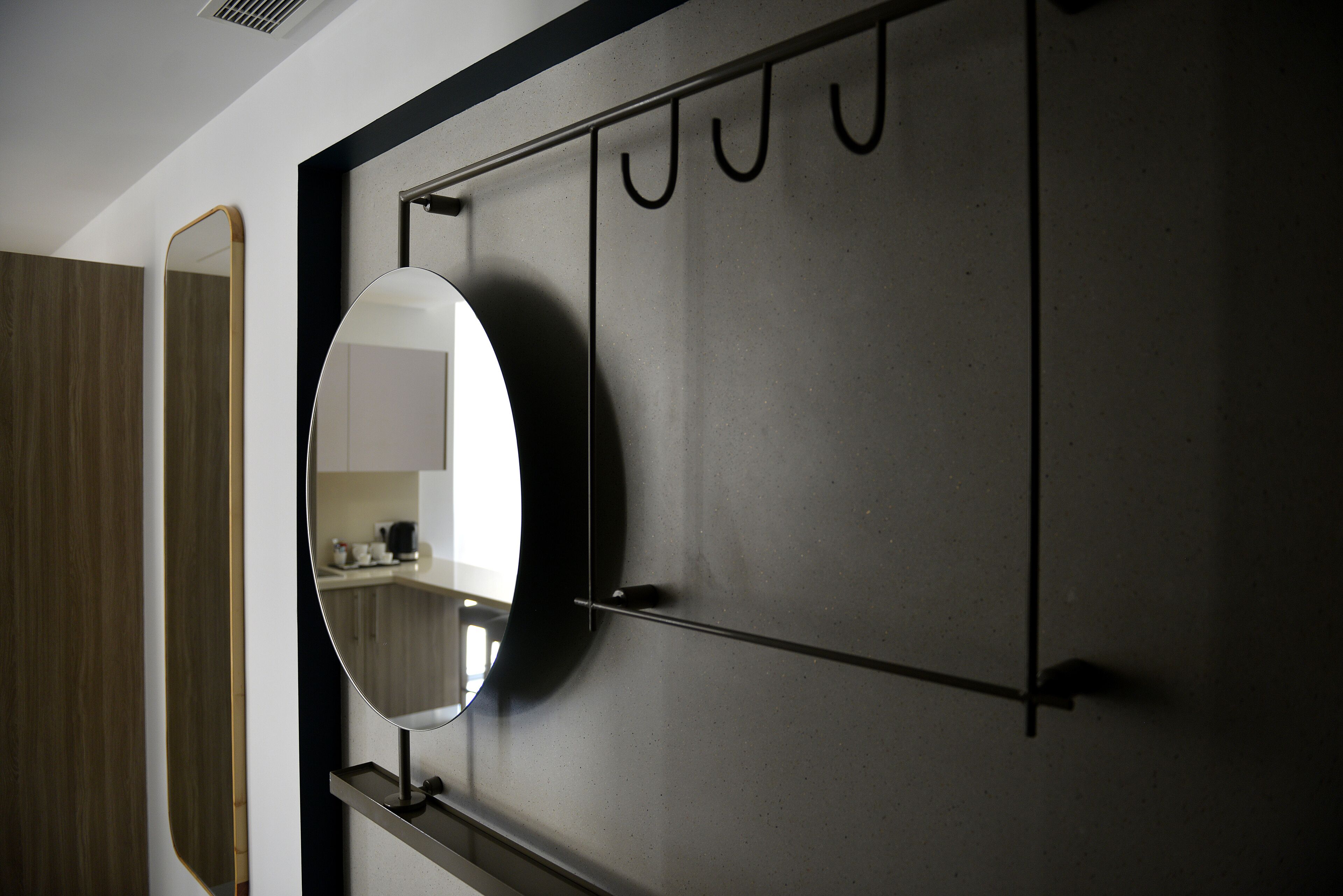 A modern bathroom with a large mirror, a towel rack, and a wooden panel on the left.