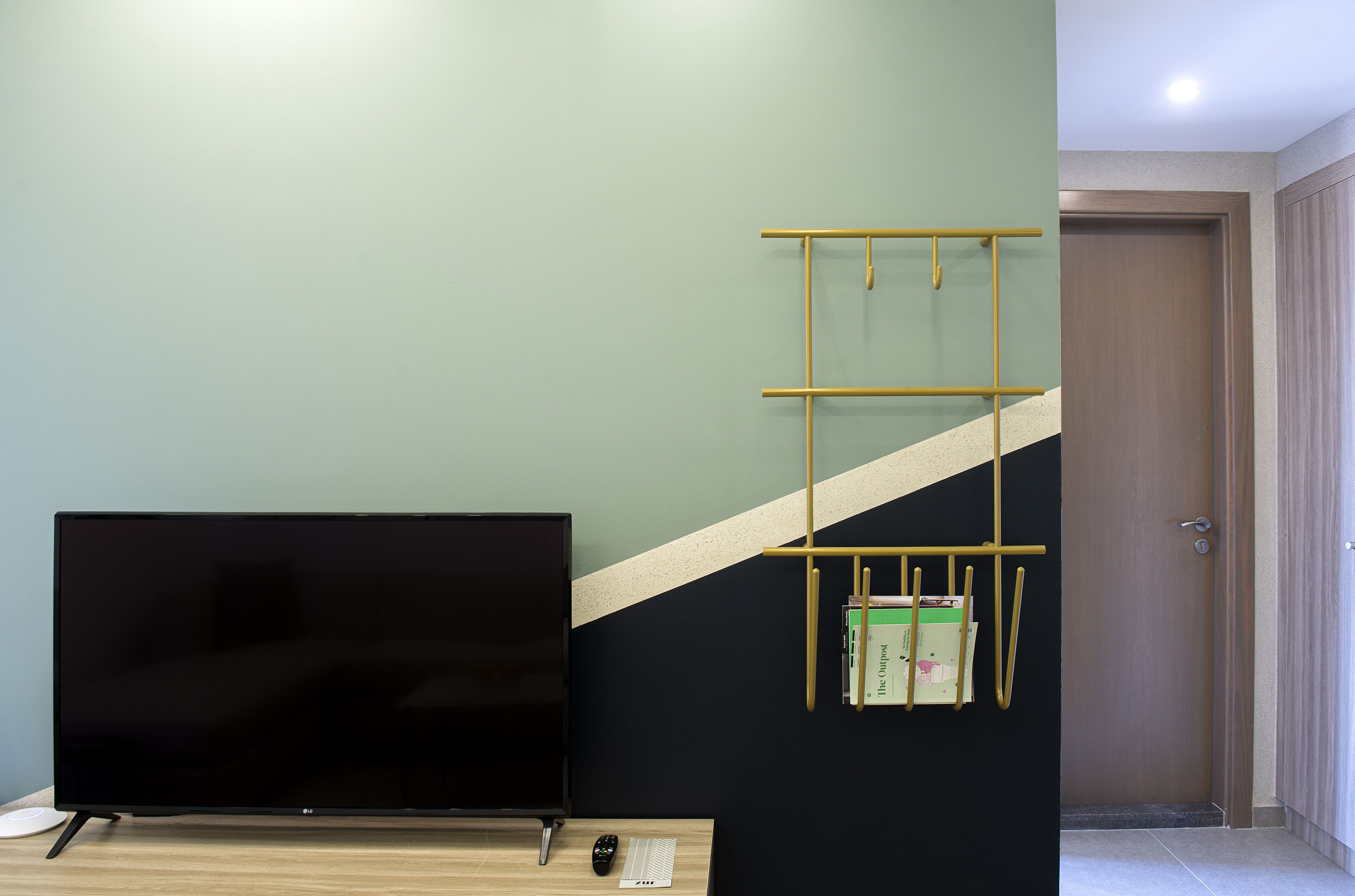 Habitación con una televisión de pantalla plana sobre una mesa de madera, un altavoz blanco pequeño y un estante metálico amarillo con libros y papeles.