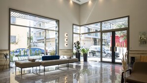 Un moderno vestíbulo con suelo reflectante, ventanas amplias, un sofá y plantas en macetas.