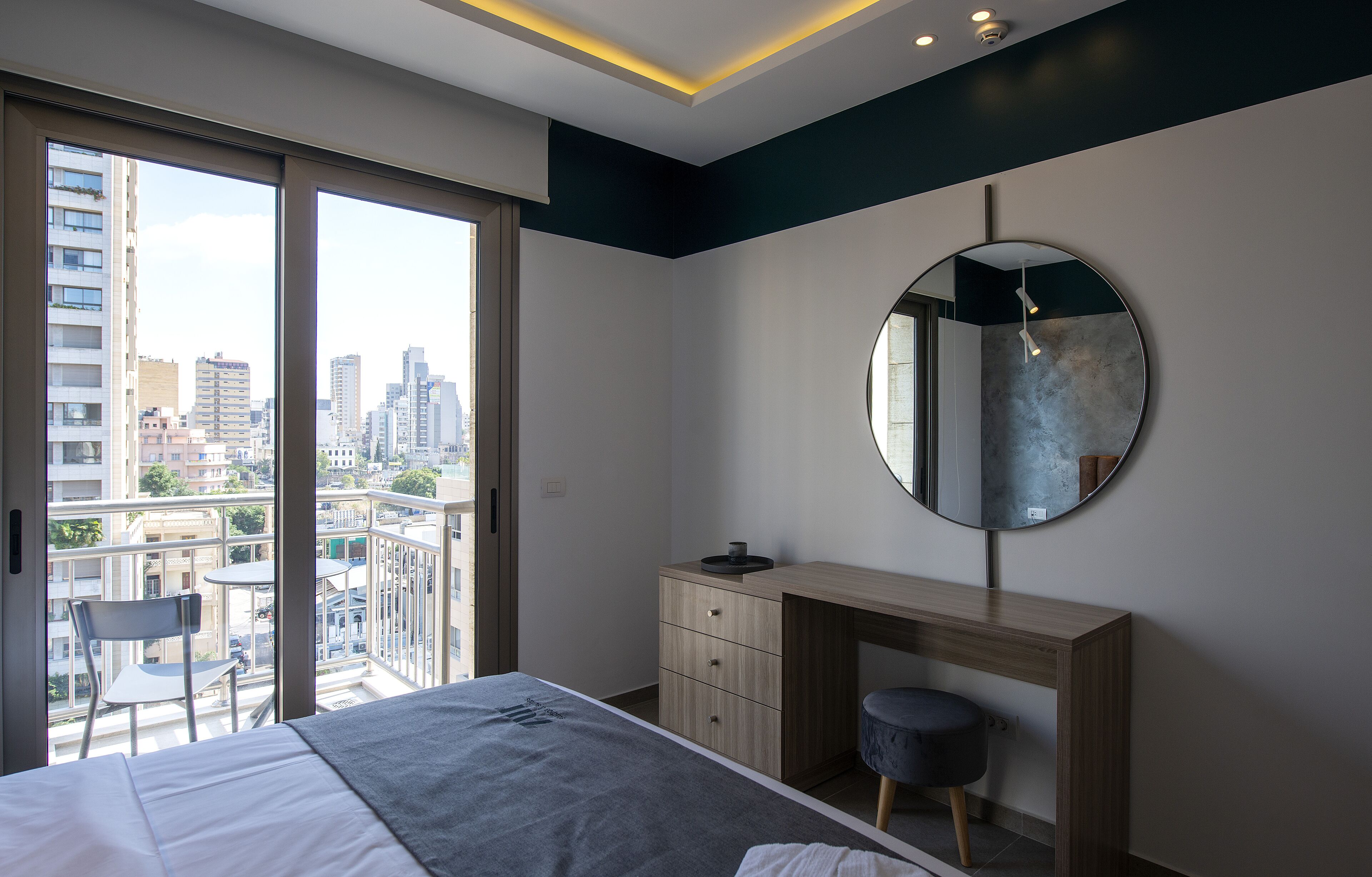 A modern bedroom with a large bed, a desk, a chair, and a round mirror.