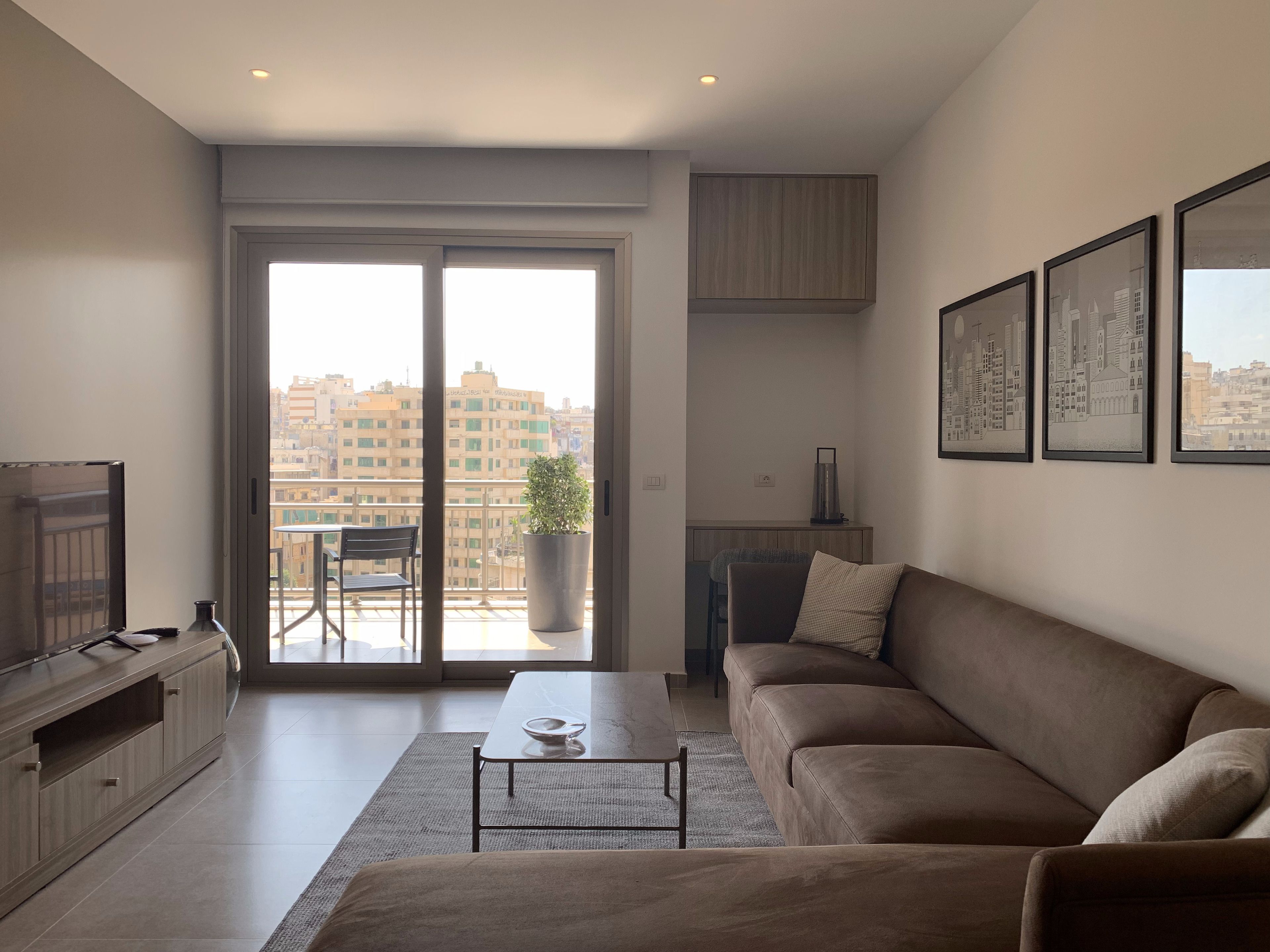 A modern living room with a sofa, a coffee table, a TV, and a balcony with a city view.