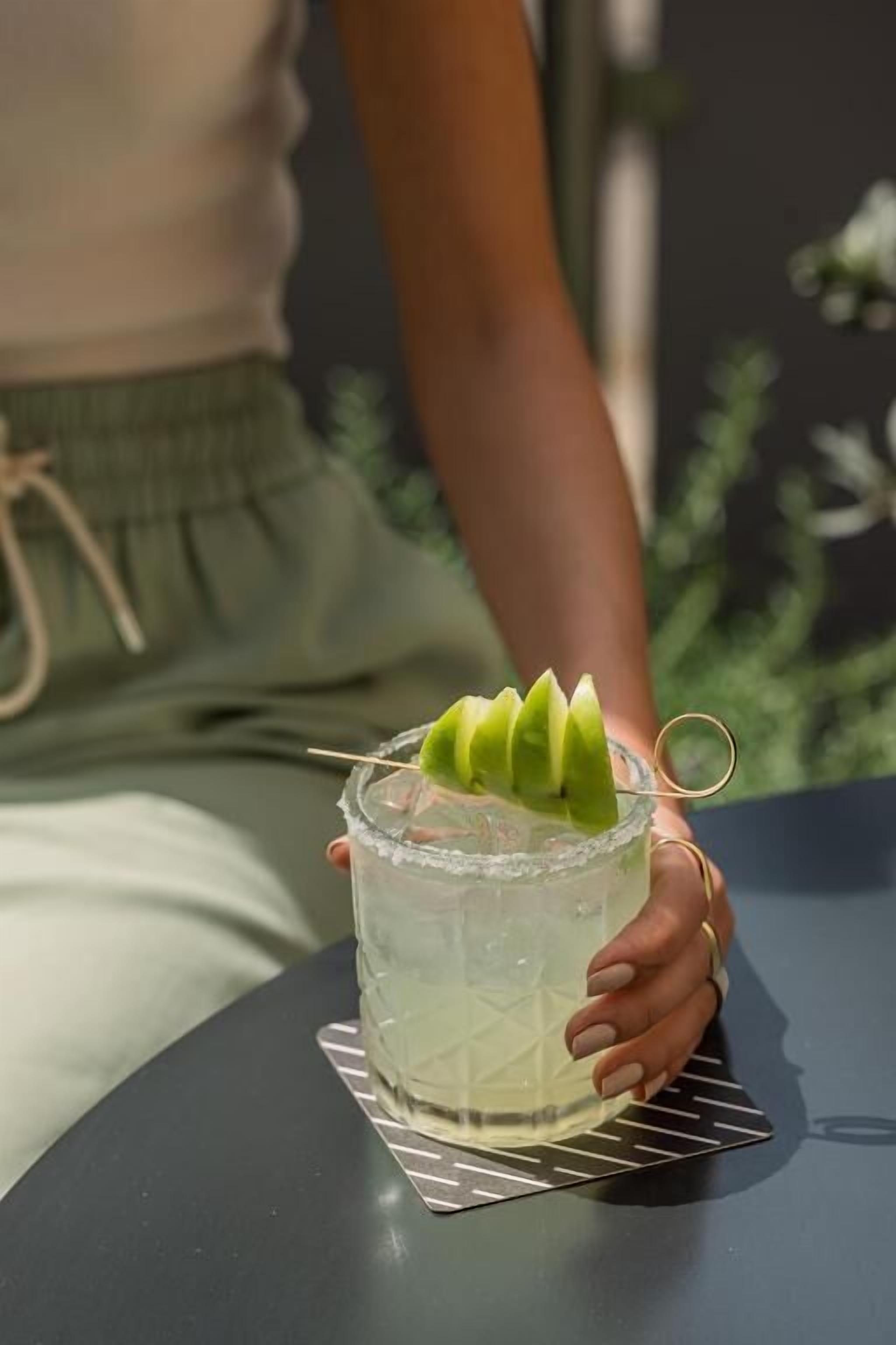 Una persona sosteniendo un vaso con una guarnición verde.