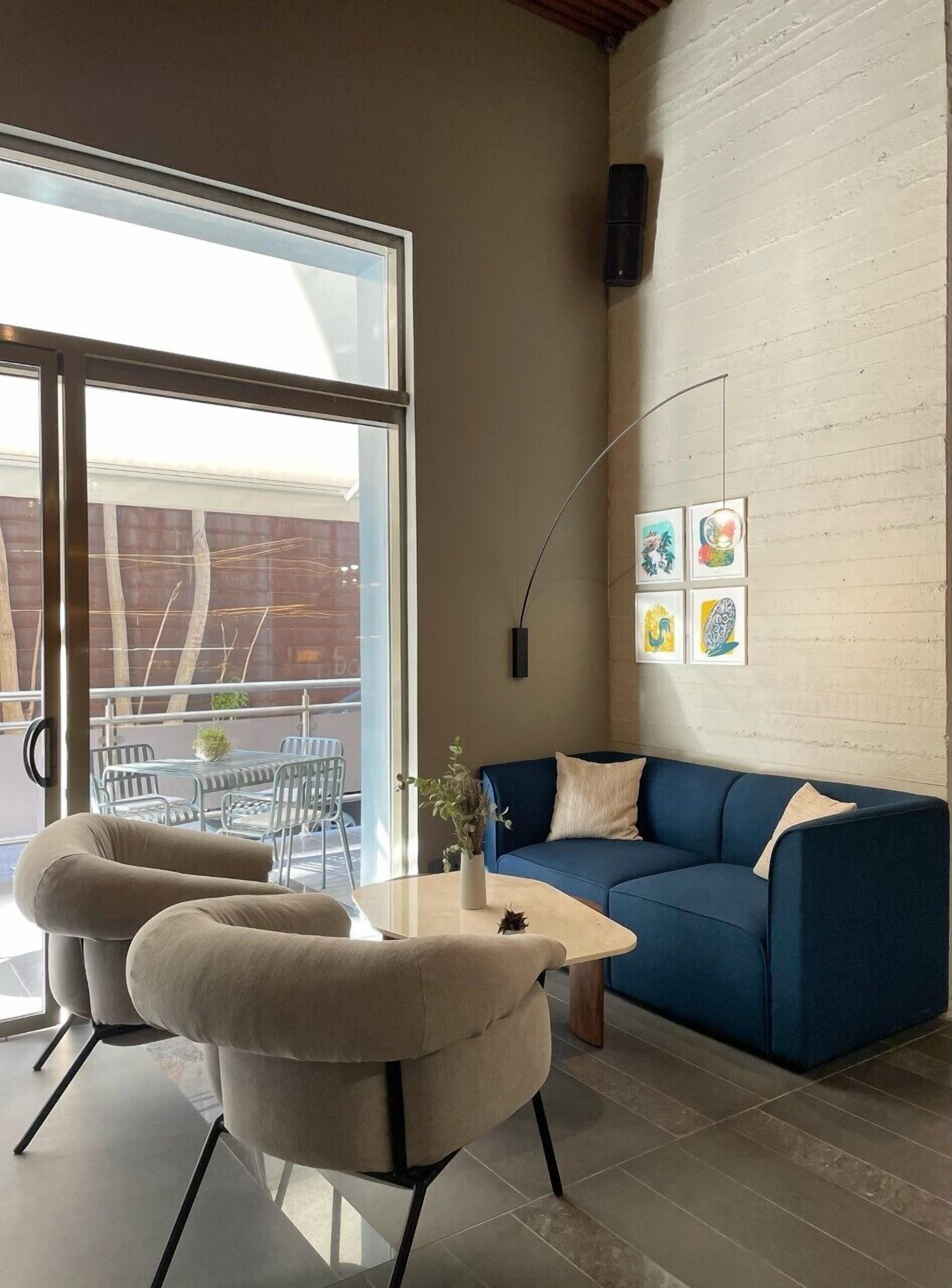 Een moderne woonkamer met een blauwe bank, twee fauteuils, een salontafel en een groot raam.