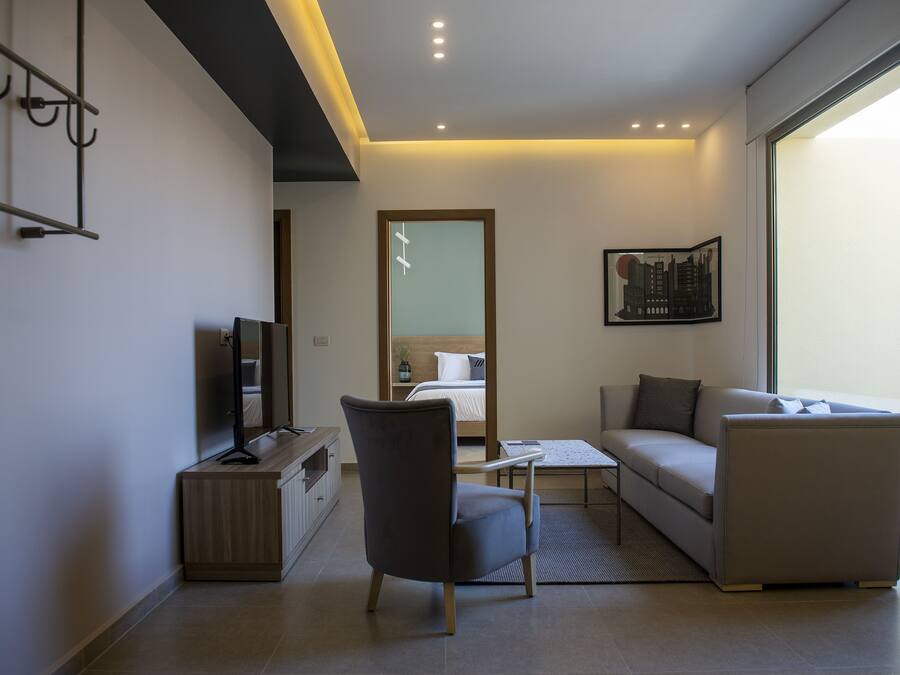 Een moderne hotelkamer met een sofa, fauteuil, flatscreen-televisie en een bed met uitzicht.