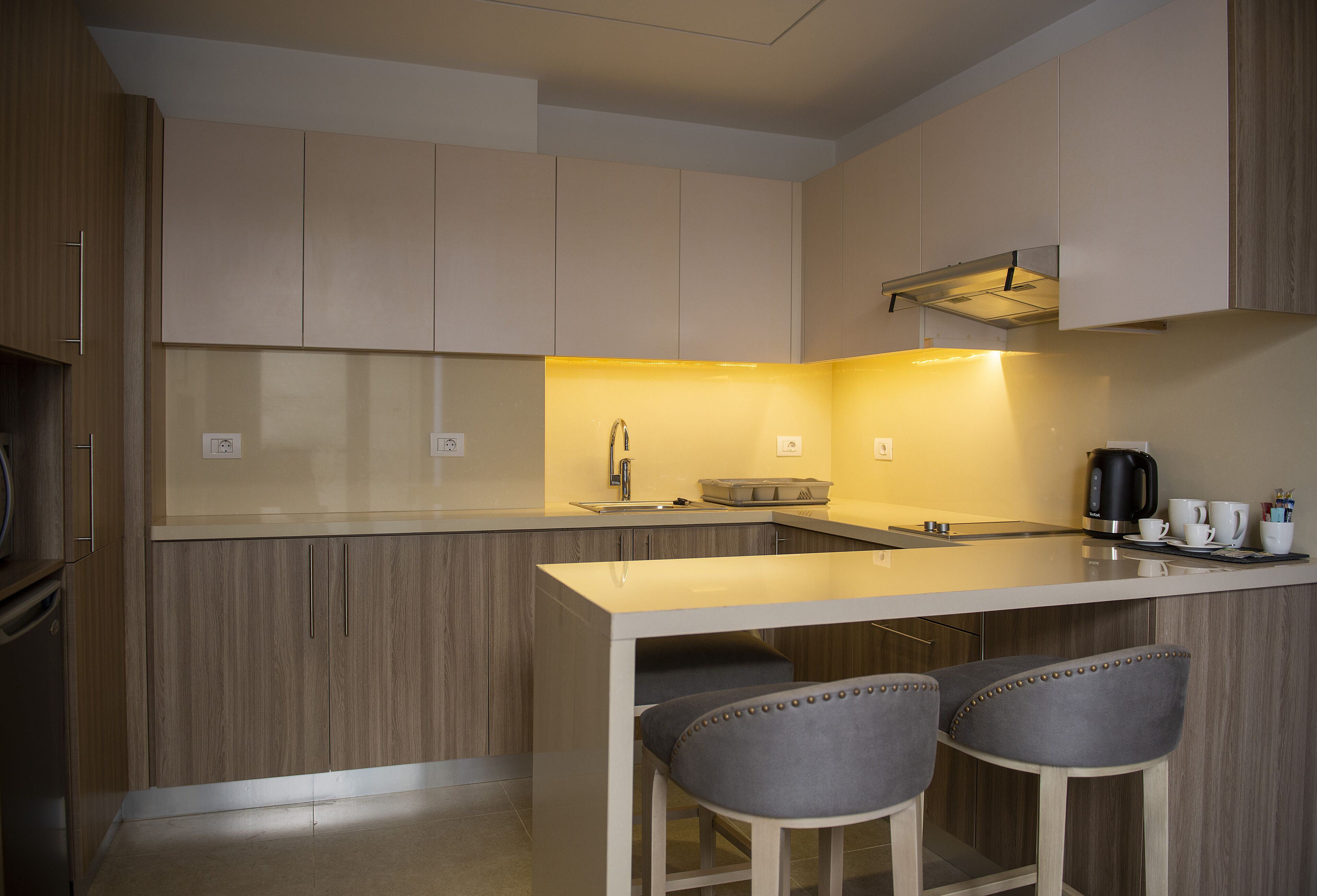 A modern kitchen with wooden cabinets, a central island with bar stools, and a coffee maker.