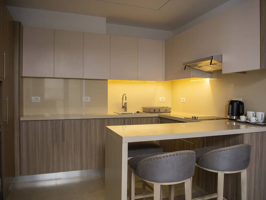 A modern kitchen with wooden cabinets, a central island with bar stools, and a coffee maker.