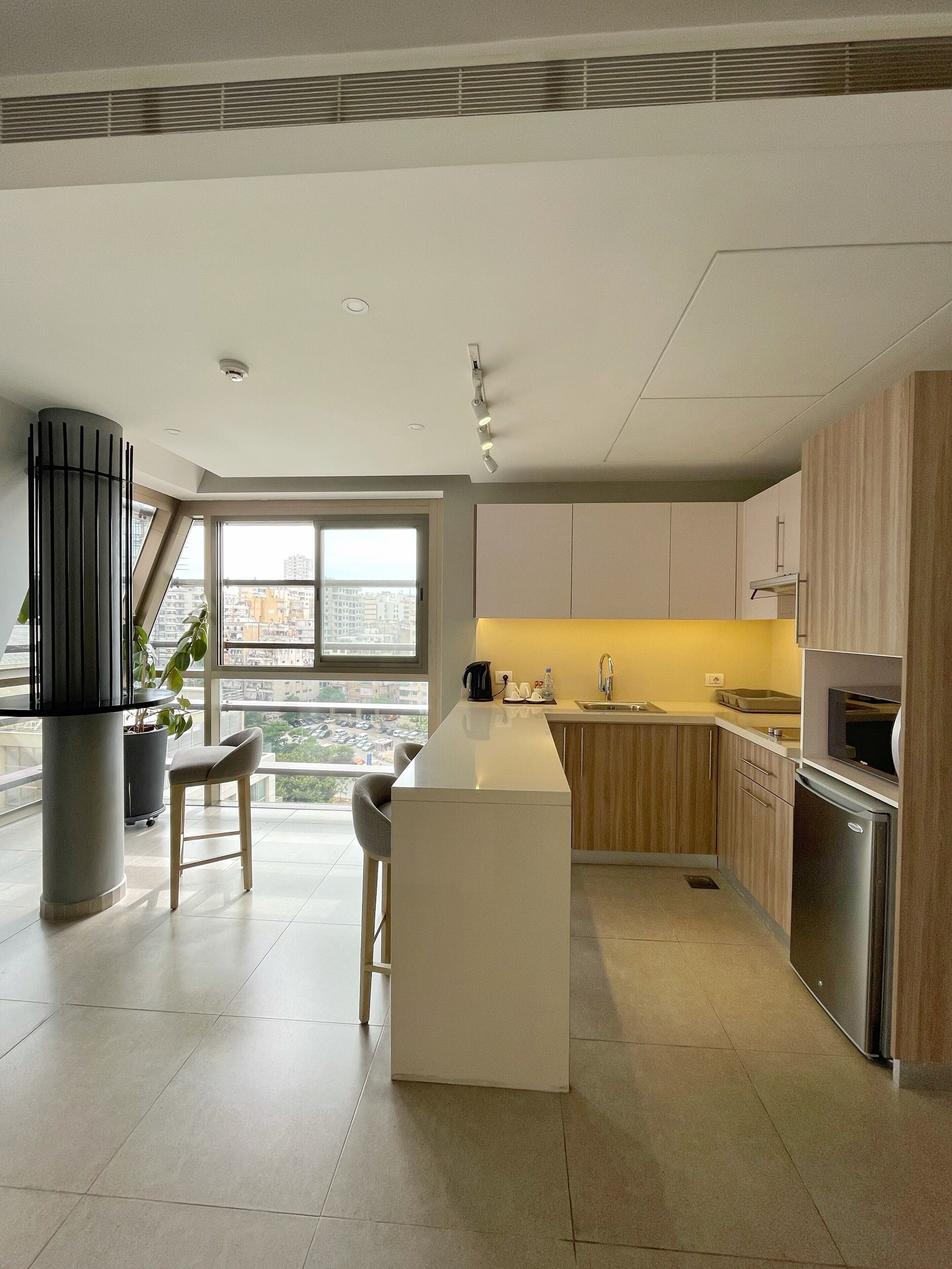 A modern kitchen with a central island, wooden cabinets, and a large window offering a city view.