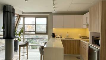 A modern kitchen with a central island, wooden cabinets, and a large window offering a city view.