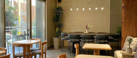A modern interior with wooden tables and chairs, a seating area with sofas, and a large window offering a view of the outside.