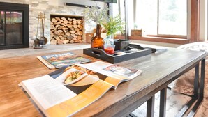 Une table de salle à manger en bois, avec des magazines, une bouteille et un vase rempli de fleurs.