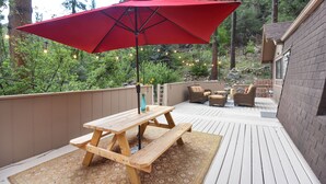 Une terrasse en bois avec une table de pique-nique et un parasol rouge, entourée d’une clôture en bois et de verdure.