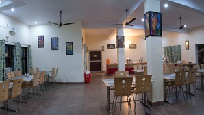 Un comedor amplio con varias mesas y sillas, ventiladores de techo y obras de arte enmarcadas en las paredes.
