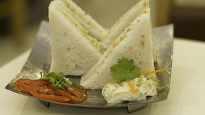 Un plato con tres sándwiches triangulares, una ensalada pequeña y una rodaja de tomate con decoración.