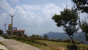 A rural road with a small building on the left, surrounded by greenery and hills in the background.