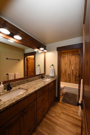 Un baño con tocador de madera, un espejo grande, un lavamanos y una bañera.
