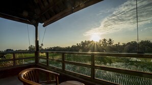 A wooden deck with a table and chairs overlooking a water body with palm trees. - Villa Tanah Carik (Tegallalang)
