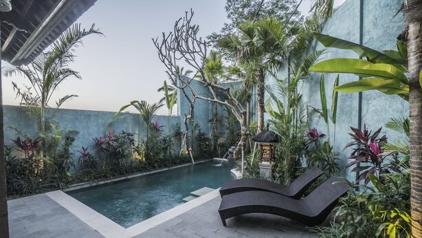 A pool area with a lounge chair, surrounded by tropical plants and a blue wall. - Villa Tanah Carik (Tegallalang)