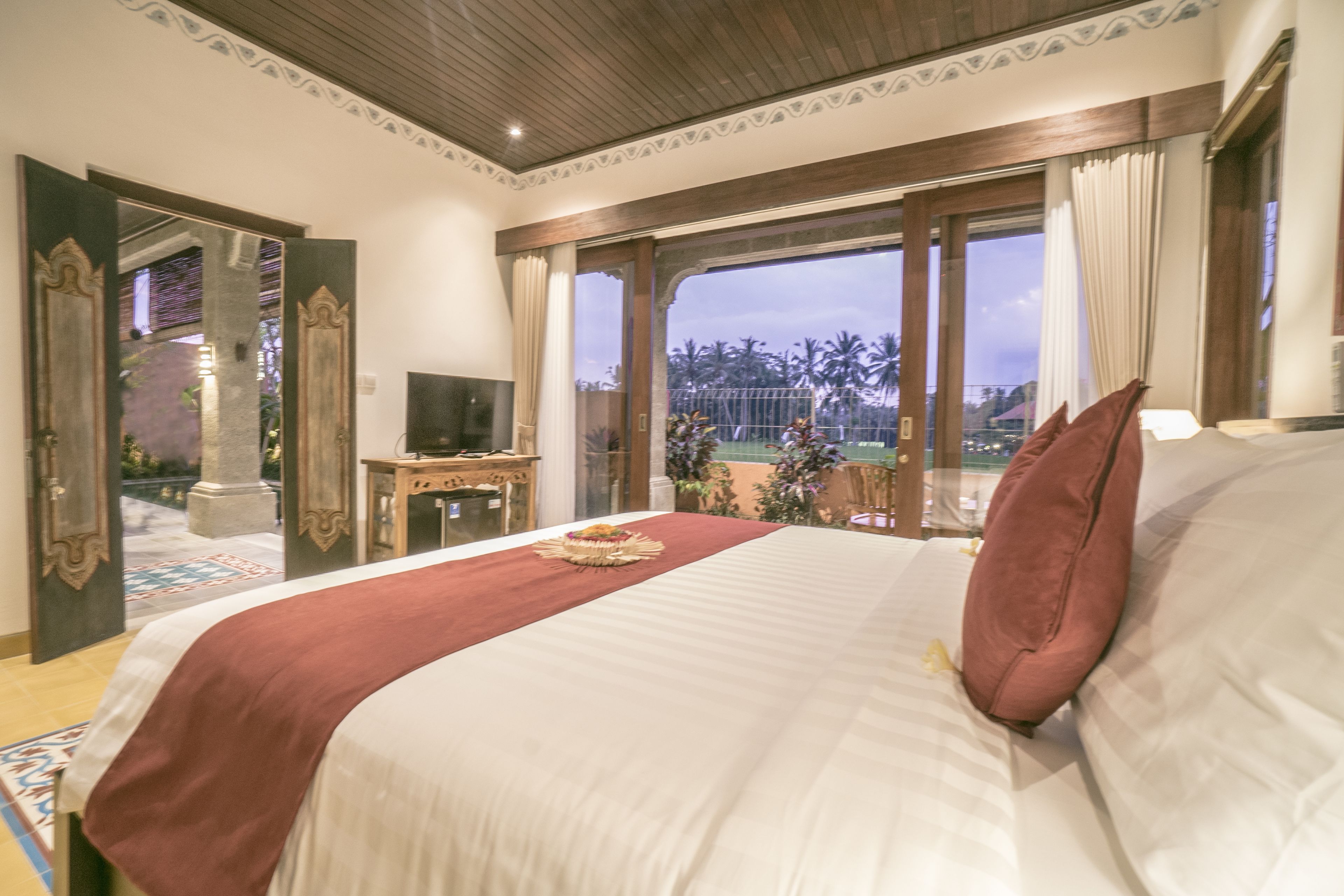 A hotel room with a large bed, a TV, and a view of palm trees.