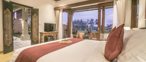 A hotel room with a large bed, a TV, and a view of palm trees.