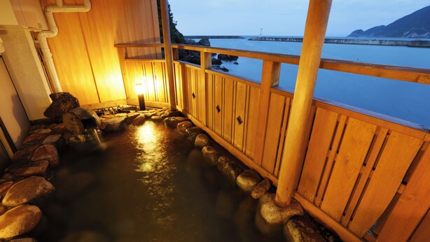 A wooden deck with a hot spring, wooden railings, and a view of the sea and mountains. - Okukinosaki Seaside Hotel (Toyooka)