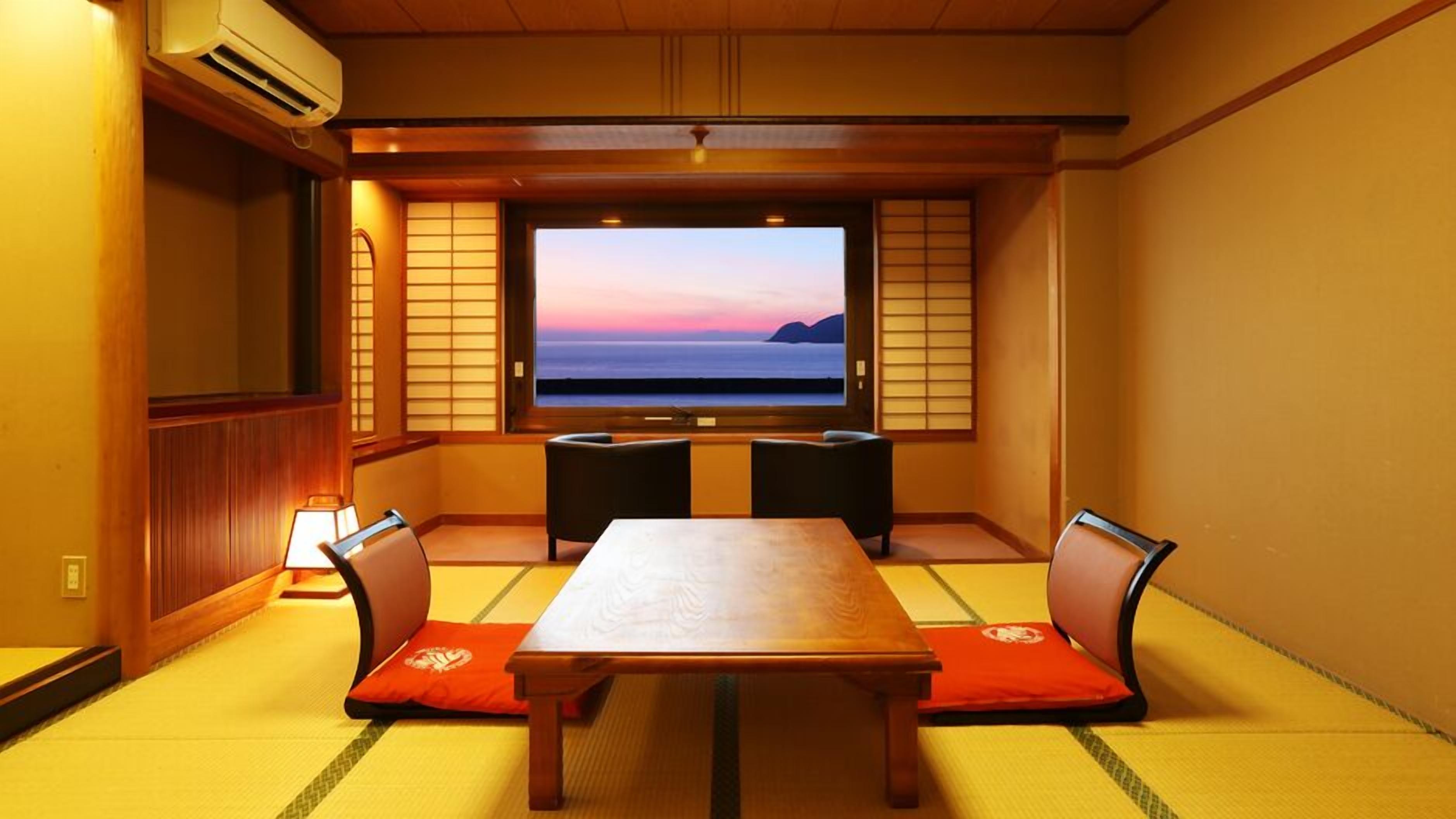 Ett traditionellt japanskt rum med tatamimattor på golvet, ett lågt bord och en tv-skärm som visar en solnedgång.