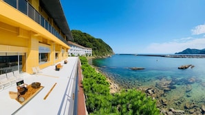 A coastal hotel with a balcony overlooking clear blue waters and a rocky shoreline. - Okukinosaki Seaside Hotel (Toyooka)
