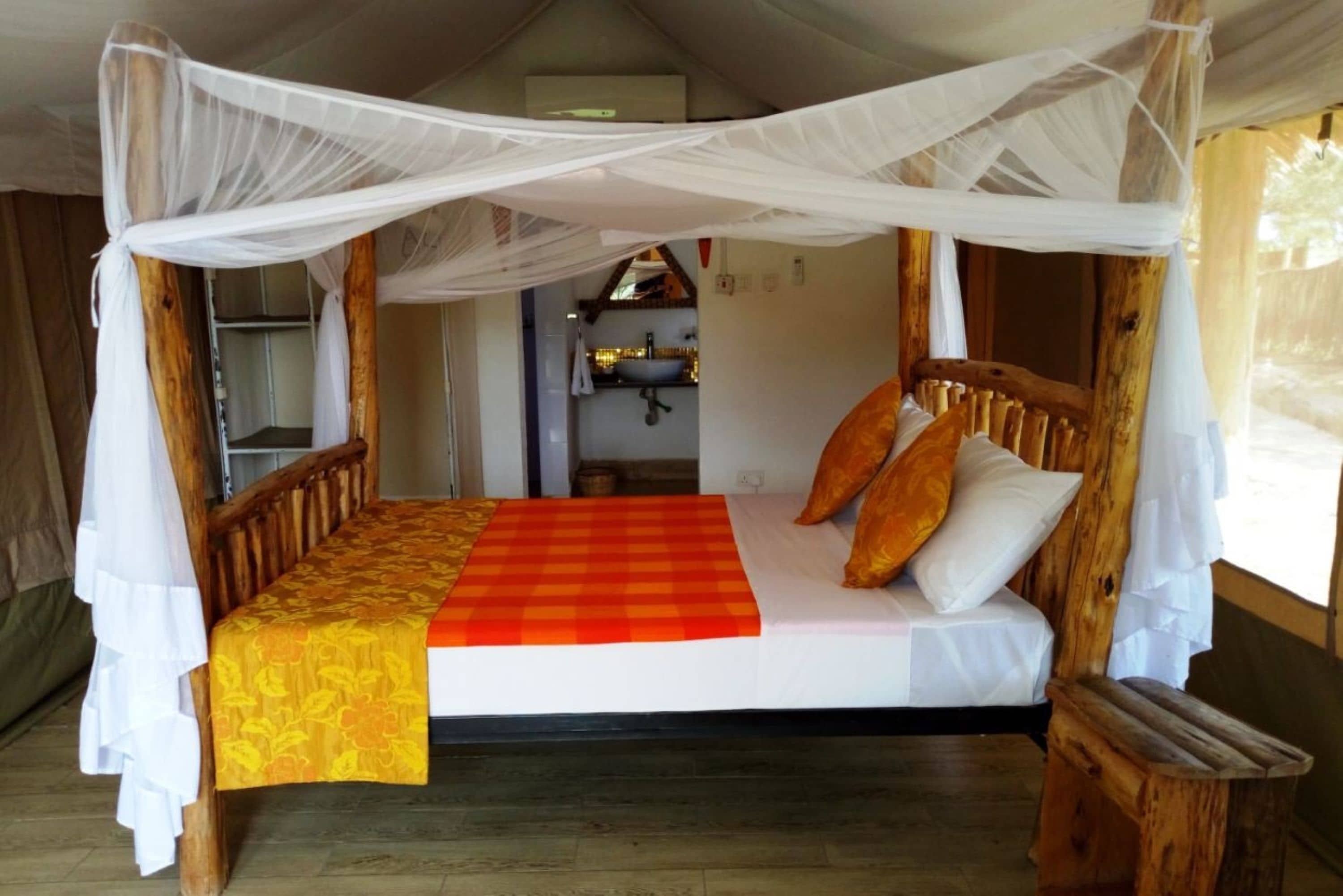 Una cama con dosel de madera, cubierta con un edredón a cuadros rojo y amarillo, y almohadas blancas.