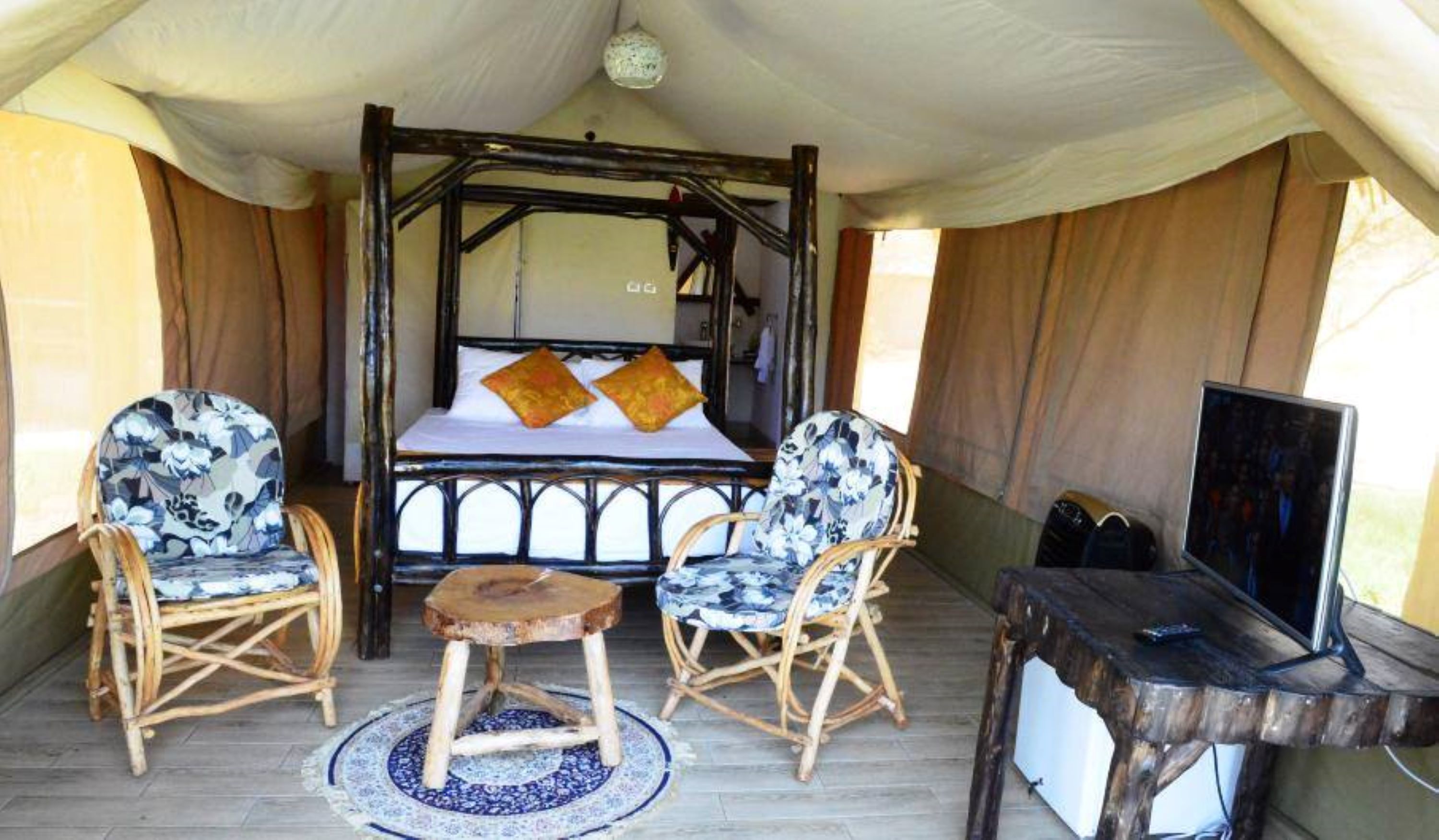 A tented room with a bed, two chairs, a small table, and a TV.