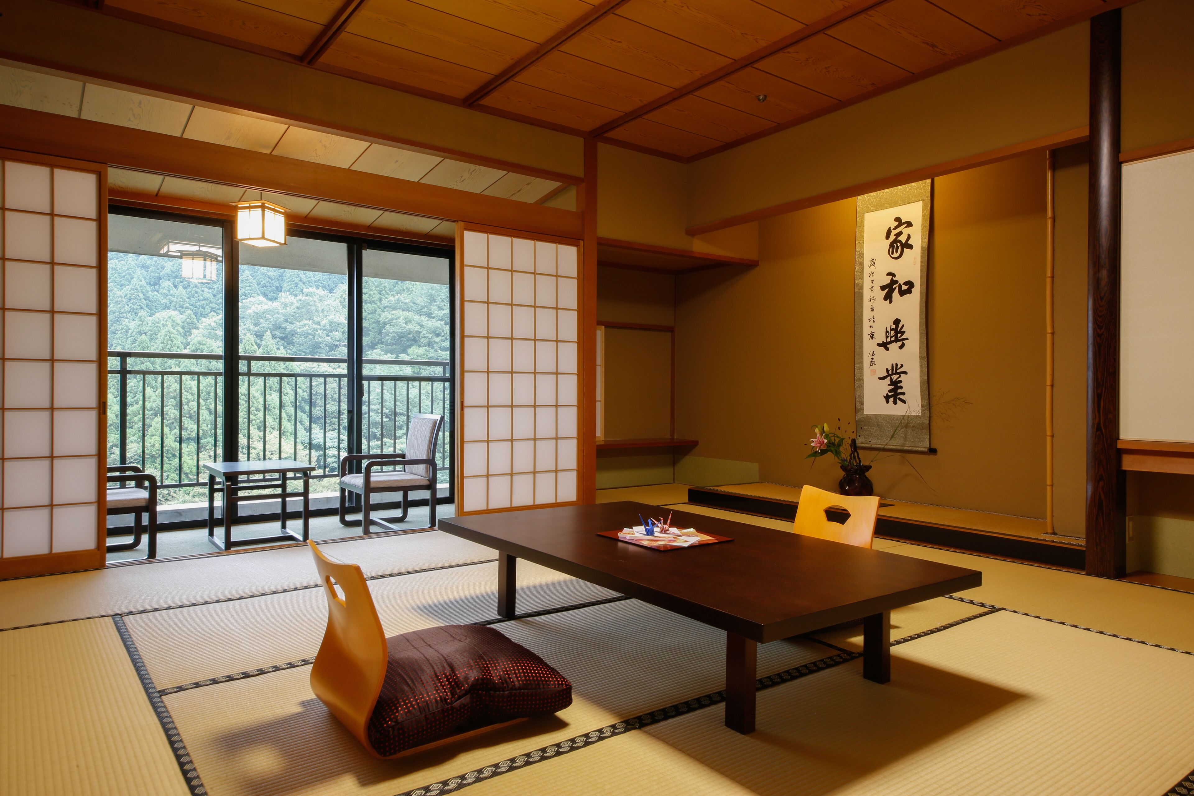 Una habitación tradicional japonesa con suelo de tatami, una mesa baja y puertas correderas que dan a un balcón con vistas a árboles.