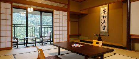 Una habitación tradicional japonesa con suelo de tatami, una mesa baja y puertas correderas que dan a un balcón con vistas a árboles.