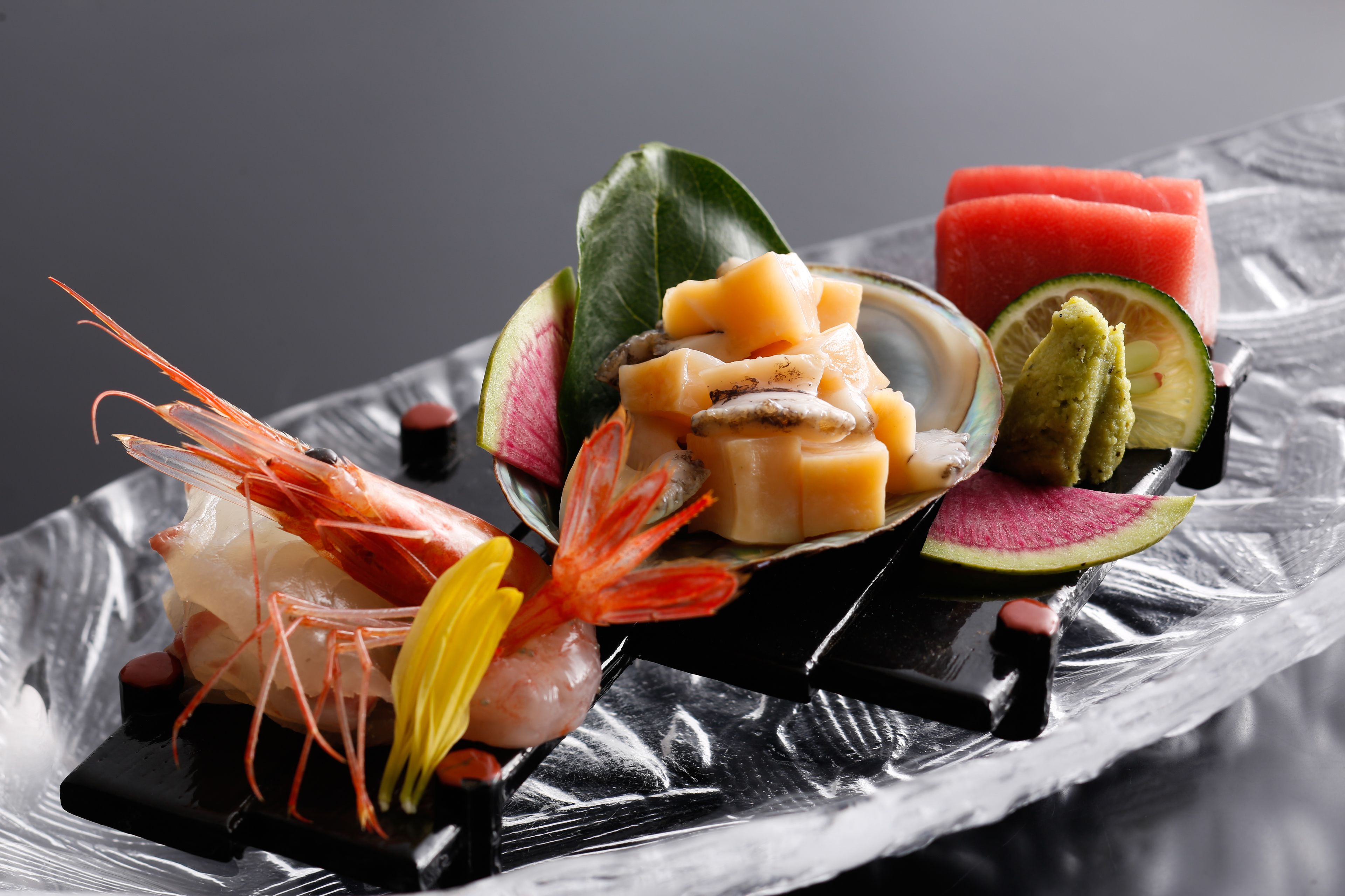 Variedad de mariscos y frutas dispuestas sobre una bandeja negra.