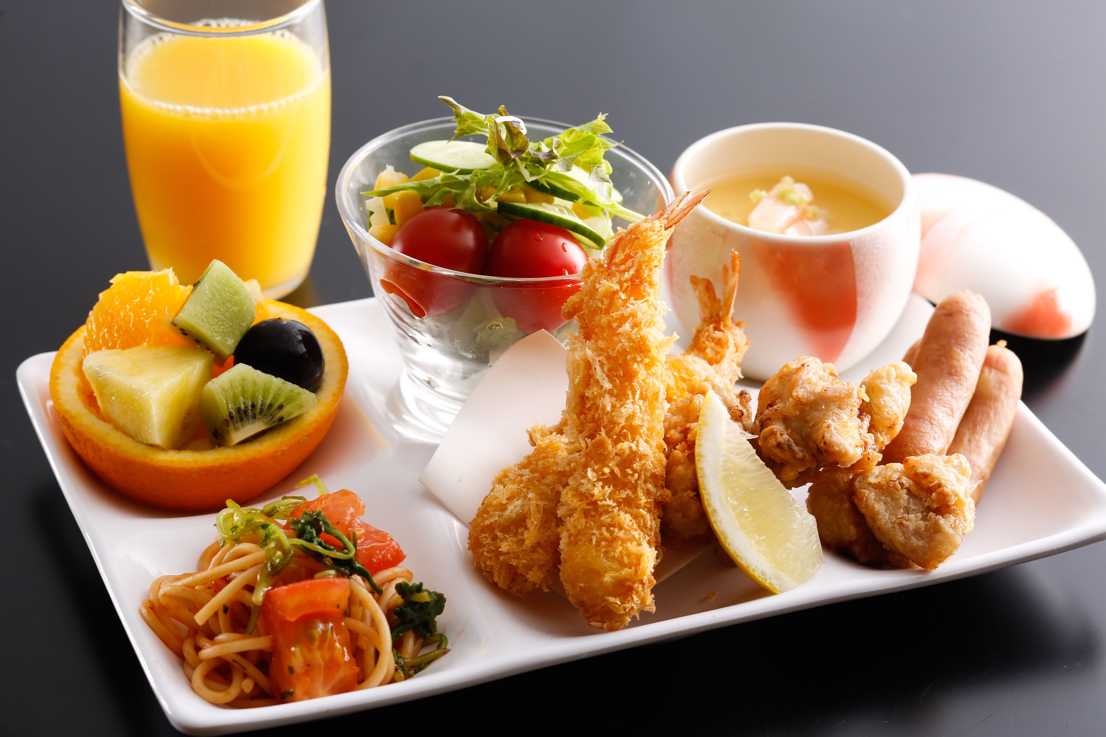 Variedad de platos que incluyen ensalada, camarones, fideos y un vaso de jugo de naranja.