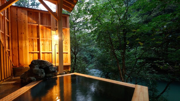 A wooden hot spring bath with a view of a forested area.