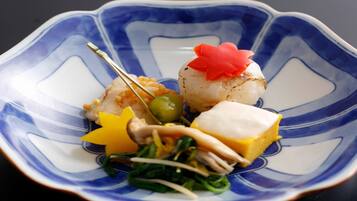 A blue and white ceramic plate with a scallop, a piece of yellow food, a green vegetable, and a red garnish.