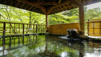 En traditionel japansk onsen med trækonstruktion, en stenhørelse og udsigt til frodigt grønt område.