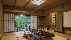 A traditional Japanese room with tatami flooring, a low table with cushions, and a sliding door leading to a balcony with a view of greenery.