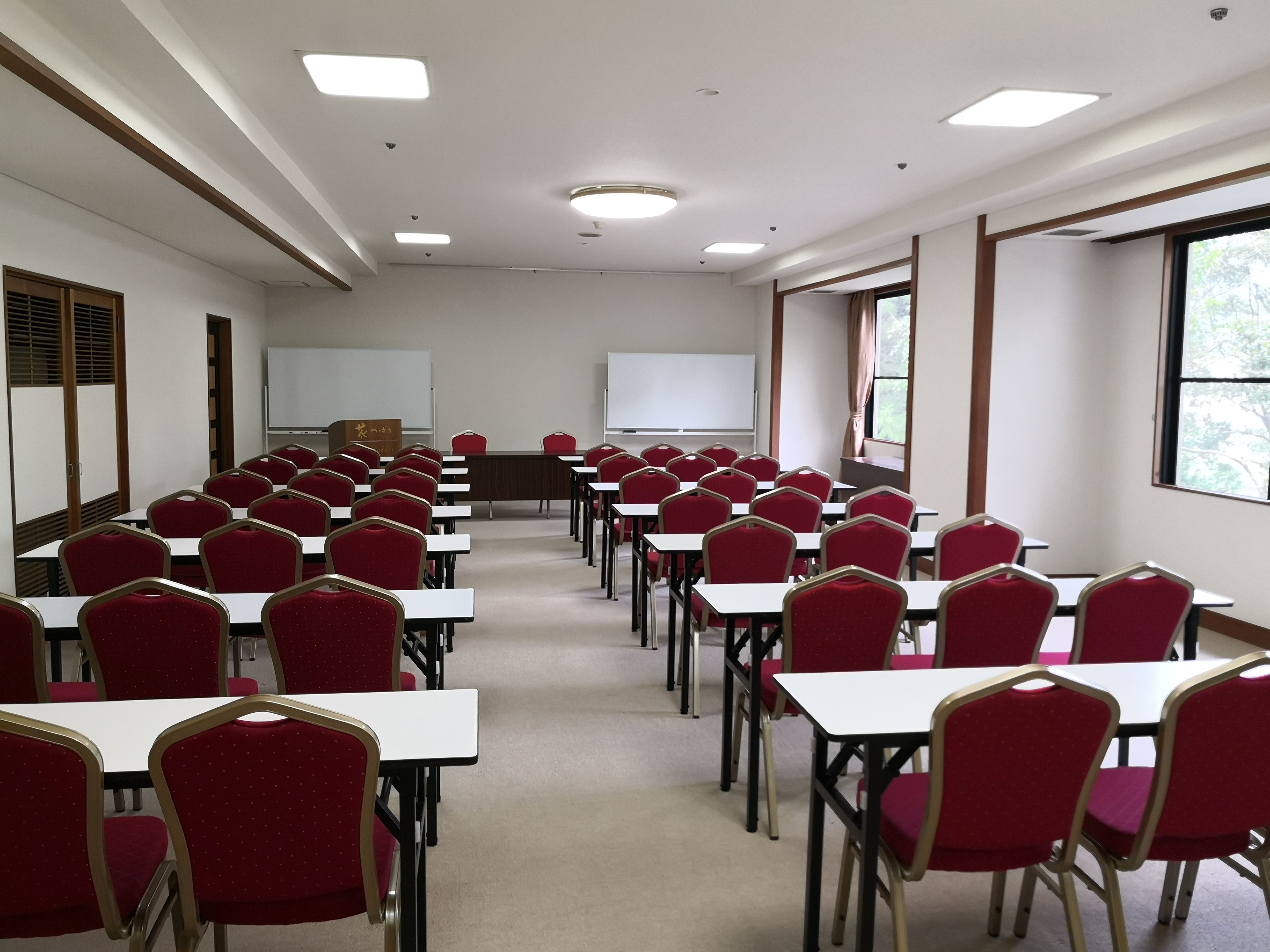 A conference room with rows of red chairs and white tables, a whiteboard, and a projector screen.