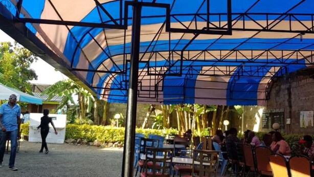 Een buitenzitplaats met tafels en stoelen onder een blauw en beige overkapping.
