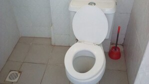 Een kleine, eenvoudige badkamer met een wit toilet, een zuiger en een toiletrolhouder.