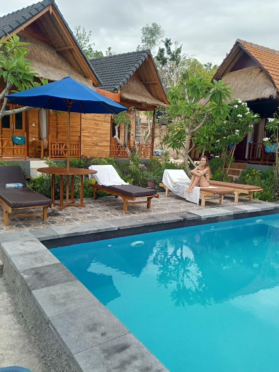 Zona junto a la piscina con cabañas de madera, sillas de descanso y sombrillas.