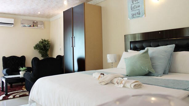 A hotel room with a large bed, a black chair, a desk, and a potted plant. - Mashamba Country House (Giyani)