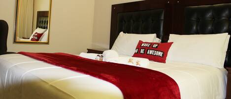 A neatly made bed with a red throw blanket, a pillow with motivational text, and a mirror on the wall.