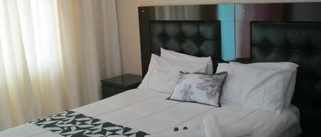 A hotel room with a bed, a nightstand, a pillow, and a blanket.