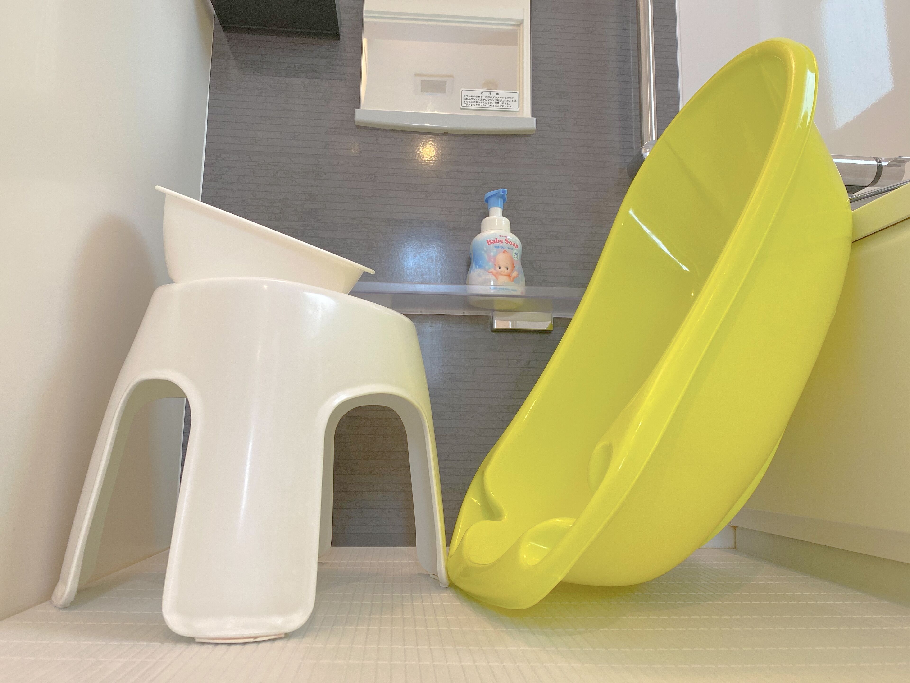 A bathroom with a yellow bathtub, a white stool, and a baby soap dispenser on a shelf.