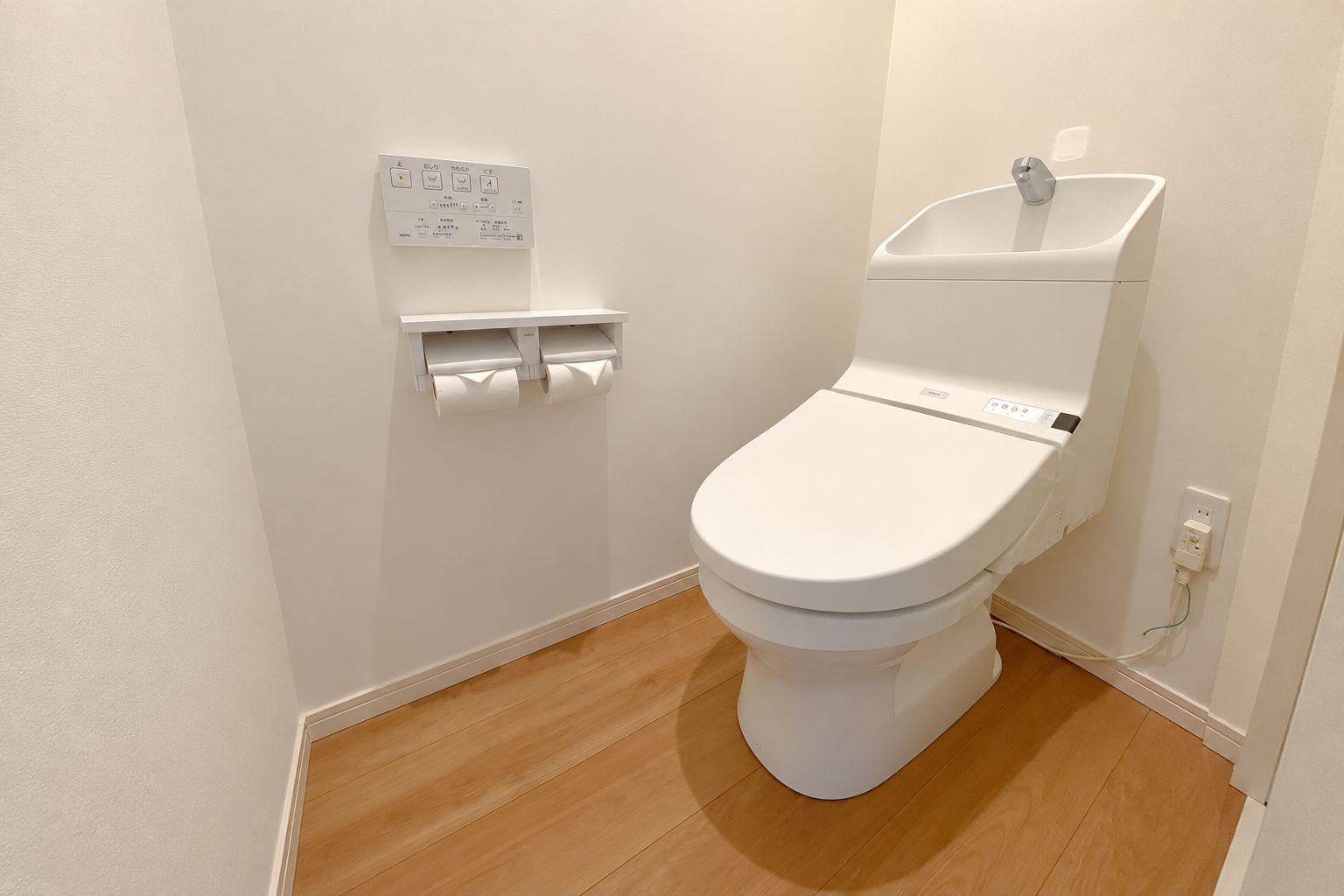 A white toilet with a flush handle, a toilet paper holder, and a control panel on the wall.