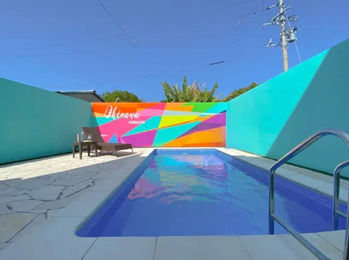 Piscina com um mural colorido ao fundo, escada de metal e área do deck revestida com azulejos.