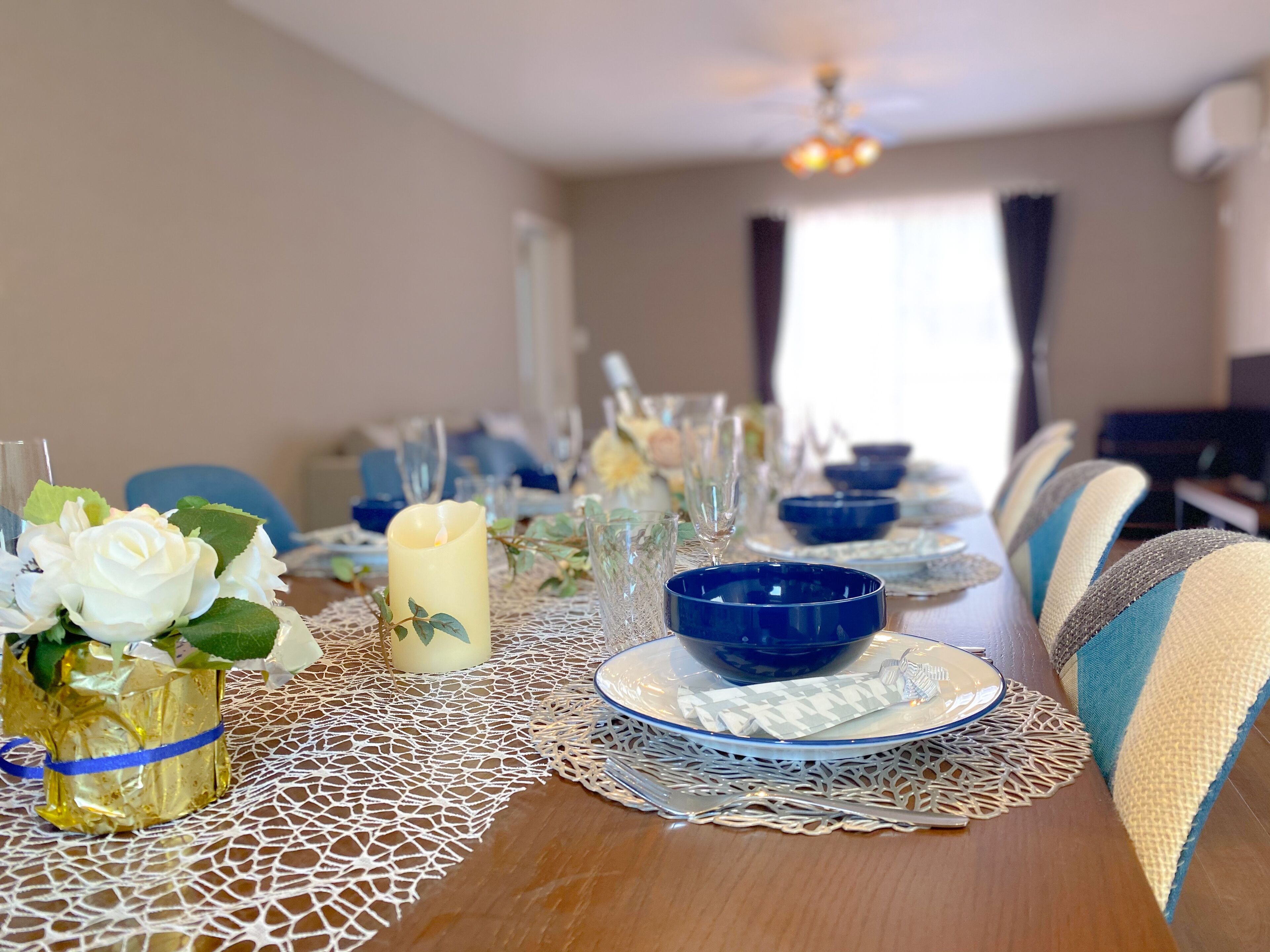 A dining table set with blue and white plates, clear glasses, and a candle centerpiece.