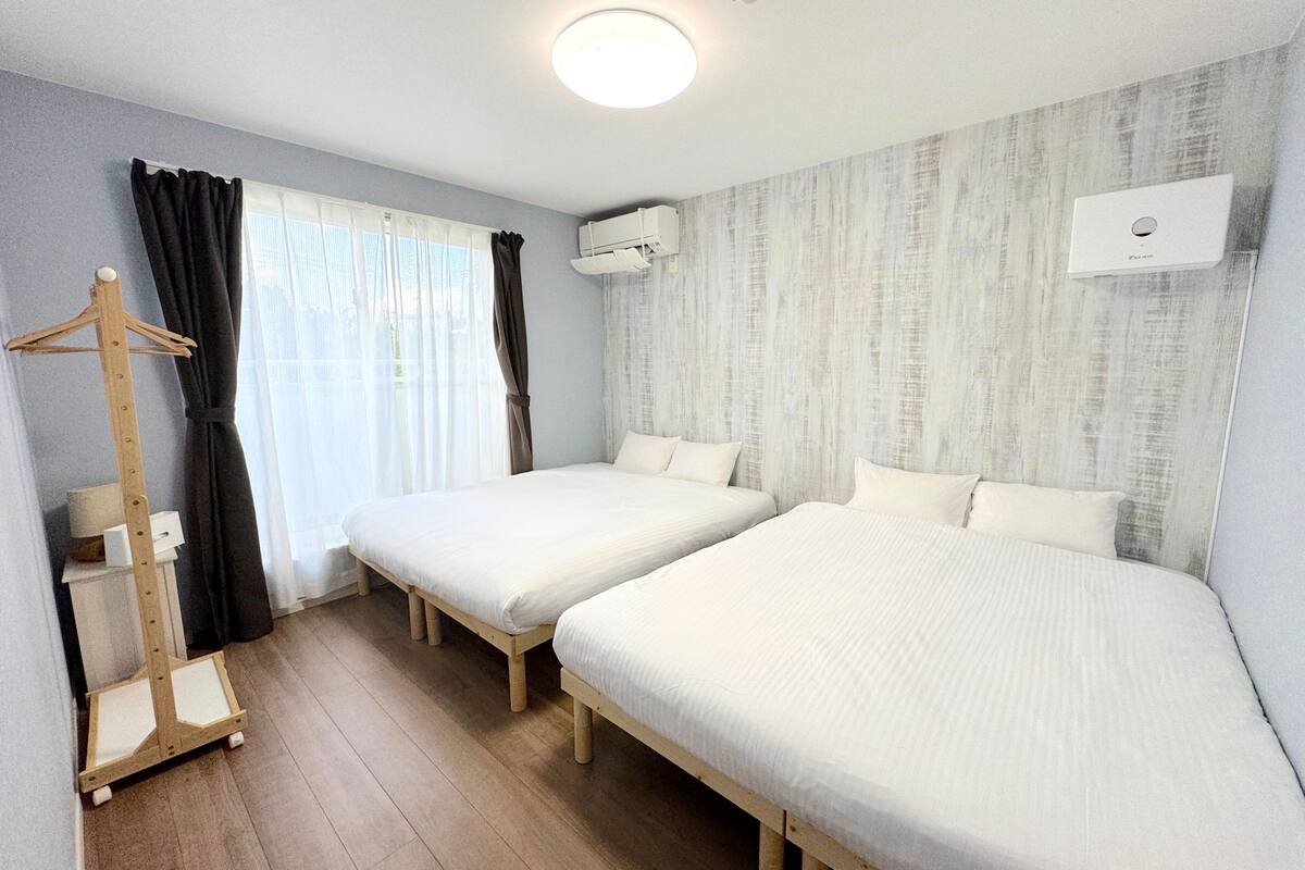 Une chambre avec deux lits simples, un porte-manteau en bois, un radiateur et un appareil de climatisation.